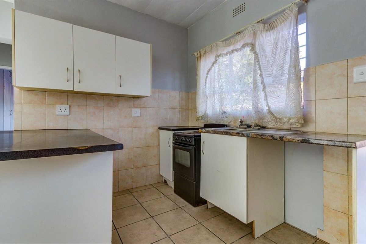 A functional kitchen featuring tiled flooring, built-in cabinetry, a tiled backsplash, and a freestanding stove, offering potential for modernization and cosmetic updates.
