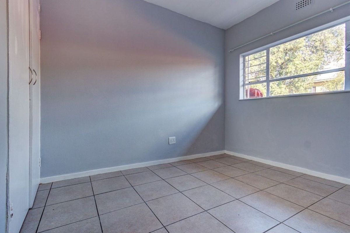 An empty bedroom featuring neutral grey walls, tiled flooring, and a built-in cupboard with security bars on the window.