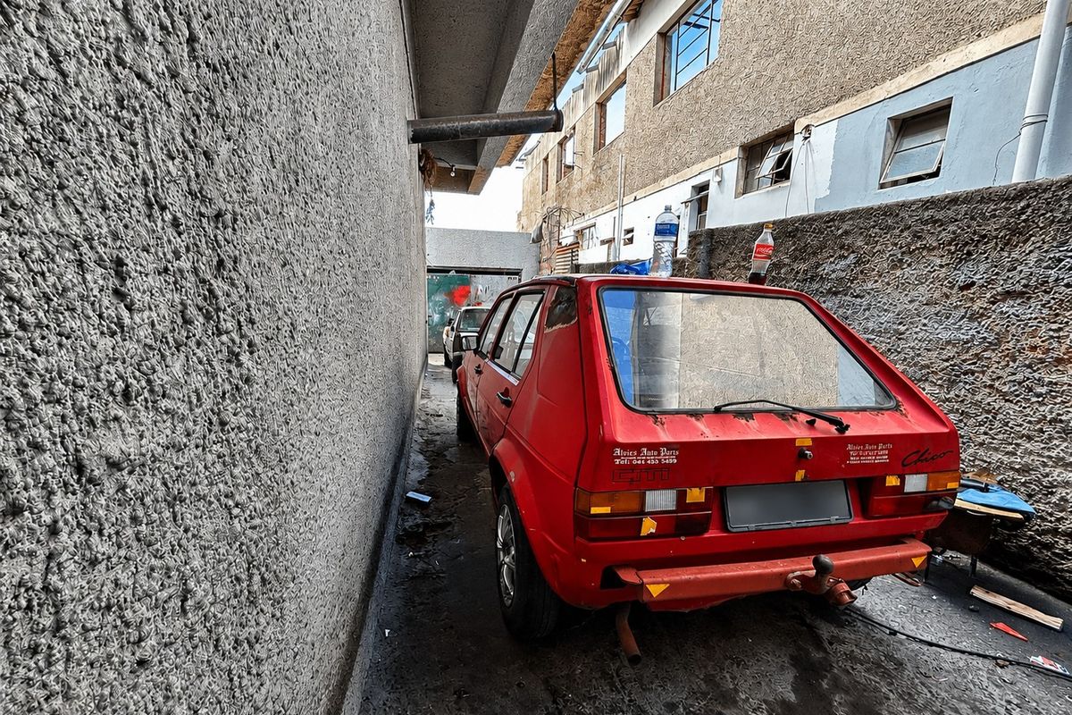 A narrow exterior side passage or rear alleyway featuring textured walls and concrete paving, currently used for vehicle storage.