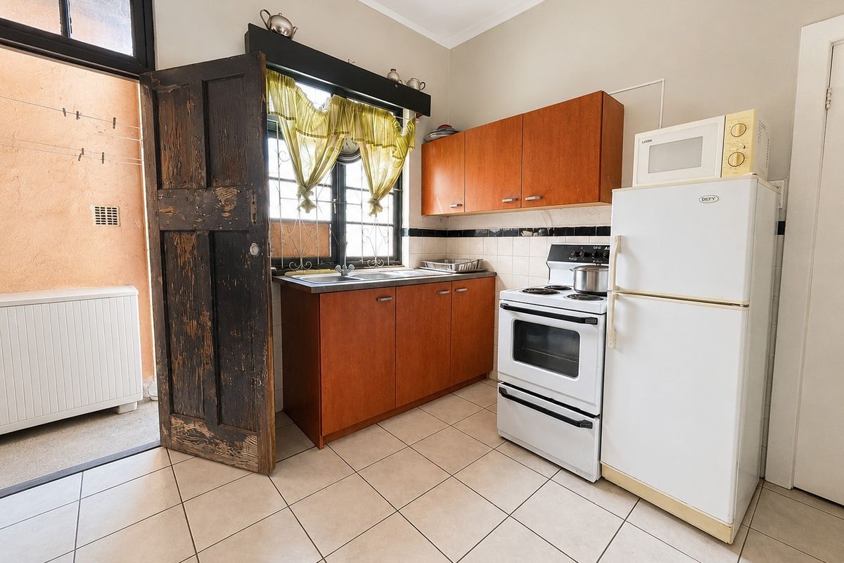 Compact kitchen featuring wooden cabinetry, tiled flooring, and a tiled backsplash, with direct access to an outdoor utility area.