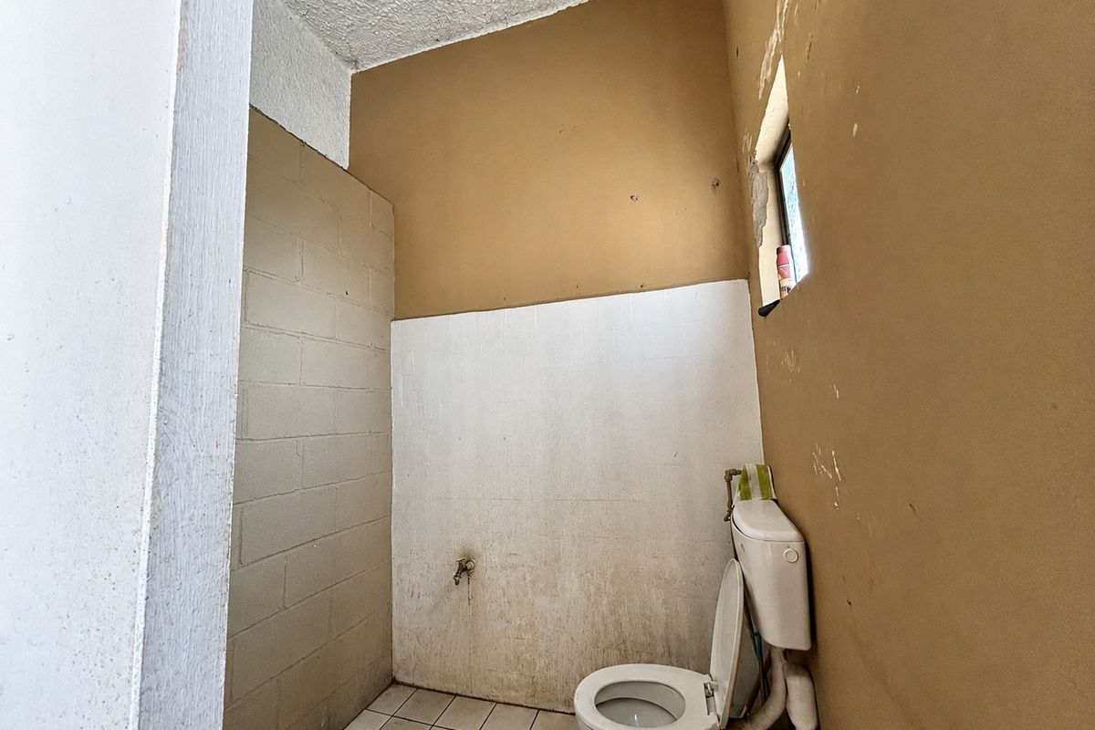 A basic bathroom featuring a toilet, tiled flooring, and exposed blockwork walls, currently in need of renovation and cosmetic updates.