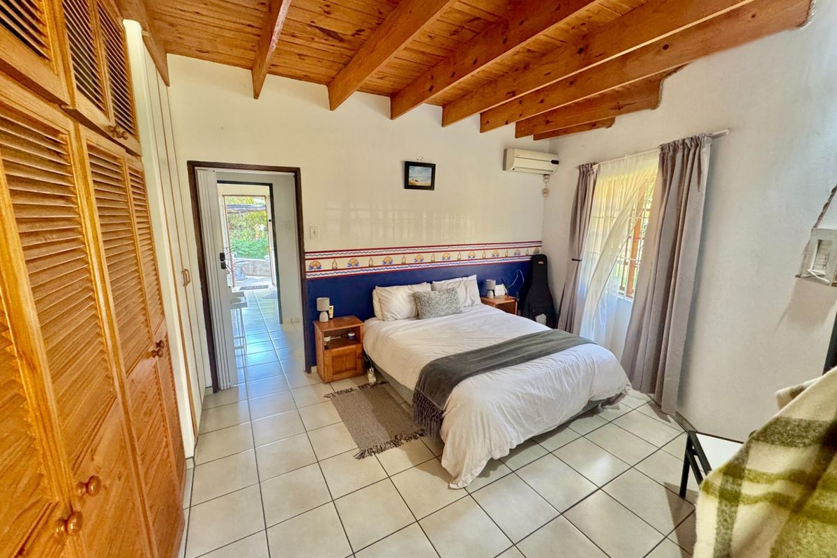 A bedroom featuring exposed timber beam ceilings, tiled flooring, and built-in wooden cupboards, with direct access to an adjoining outdoor area.