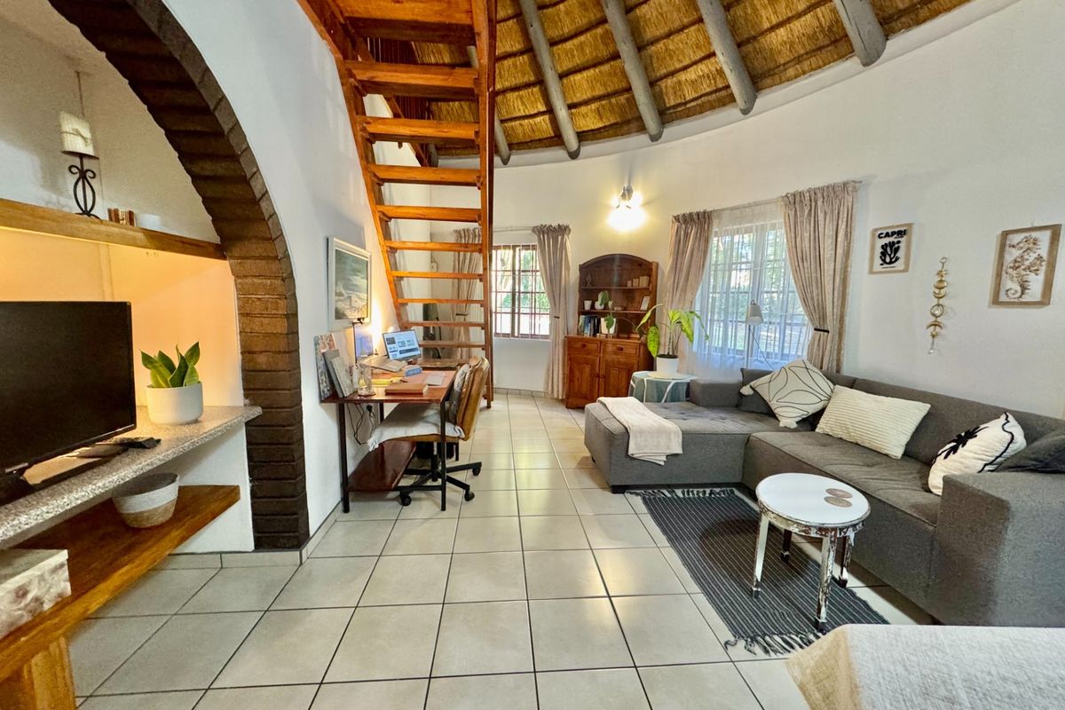 A living room featuring a unique exposed thatch ceiling, a timber staircase, and a distinctive brick archway with built-in shelving.