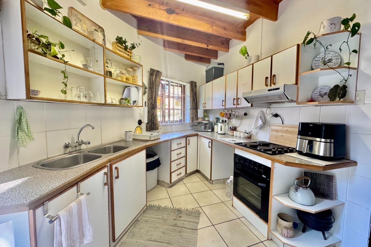 Functional kitchen featuring double bowl sink, built-in oven, hob, extractor fan, tiled splashbacks, and exposed timber ceiling beams.