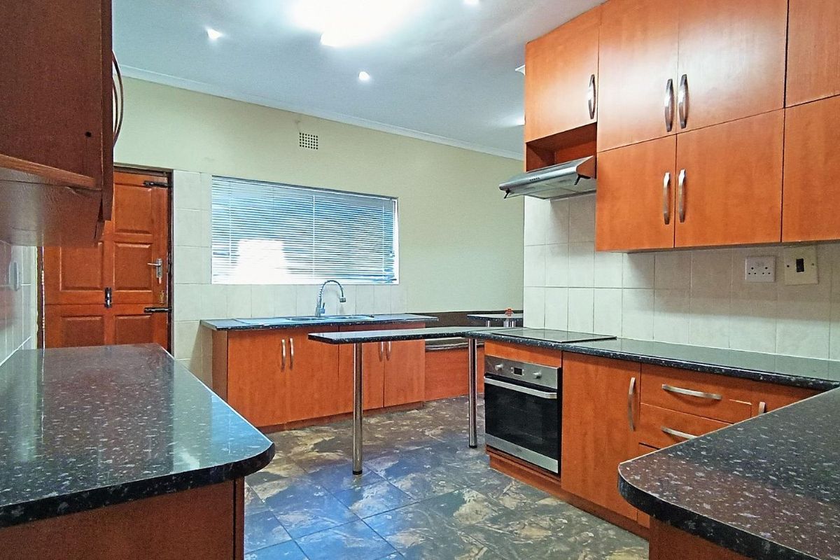 A functional kitchen featuring wood-finish cabinetry, dark laminate countertops, built-in oven and hob, and tiled flooring with a neutral backsplash.