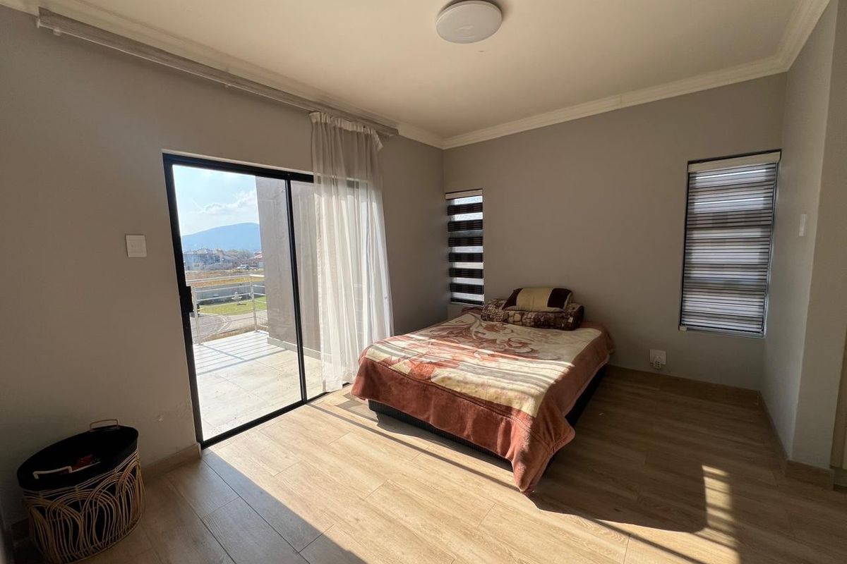 A bright bedroom featuring laminate flooring, modern zebra blinds, and a sliding glass door providing access to an outdoor balcony area.