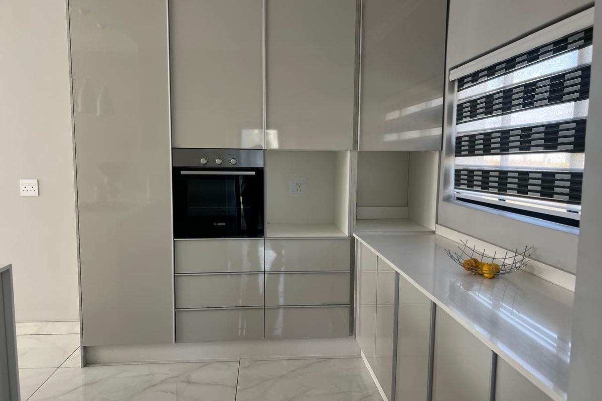 Modern kitchen featuring sleek gloss cabinetry, integrated oven, stone countertops, and polished tiled flooring with a clean, contemporary aesthetic.