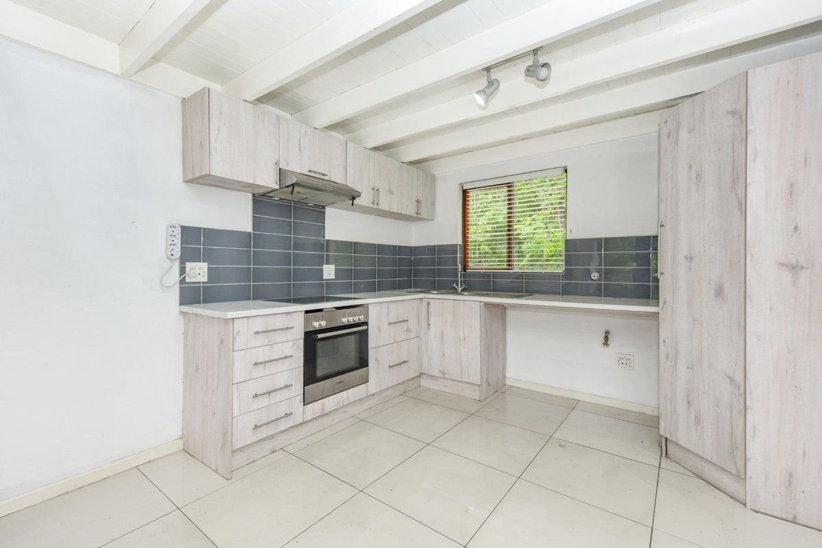 A functional kitchen featuring light wood-look cabinetry, tiled backsplash, built-in oven and hob, and exposed white ceiling beams.