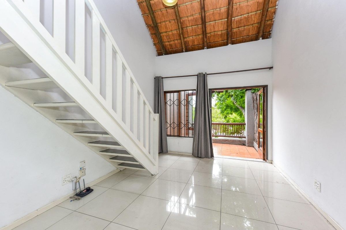 Bright living area featuring a unique thatched ceiling, tiled floors, and direct access to a balcony via a security gate.