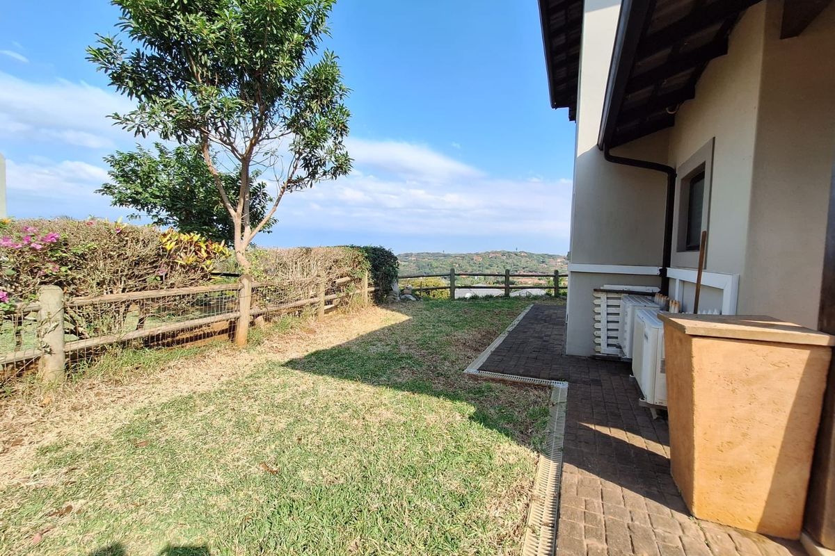 Rear garden area featuring a paved walkway, timber fencing, and scenic landscape views, with external air conditioning units installed along the building wall.