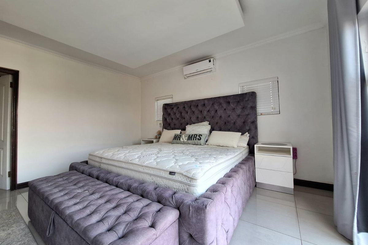 A well-maintained bedroom featuring tiled flooring, a recessed ceiling detail, and a wall-mounted air conditioning unit.