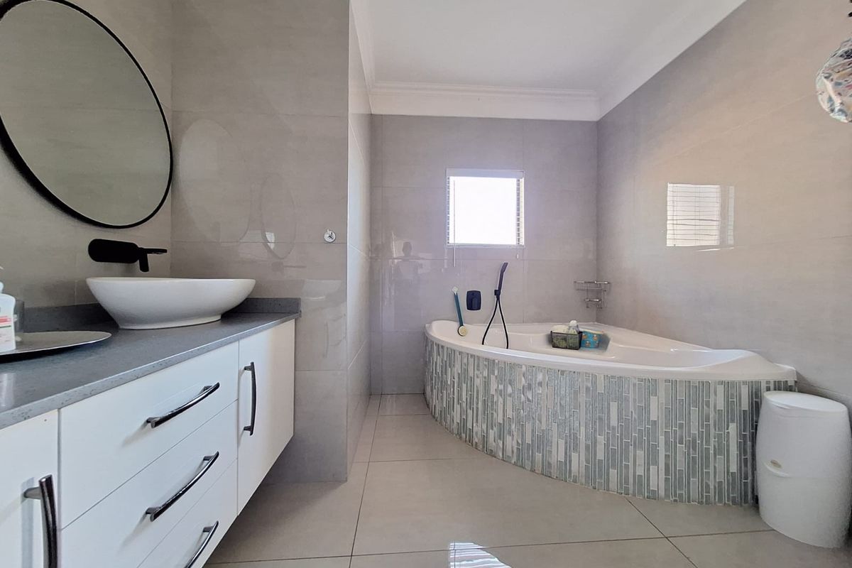 Modern bathroom featuring a corner bathtub with mosaic tiling, a sleek vanity with a countertop basin, and neutral wall and floor tiles.