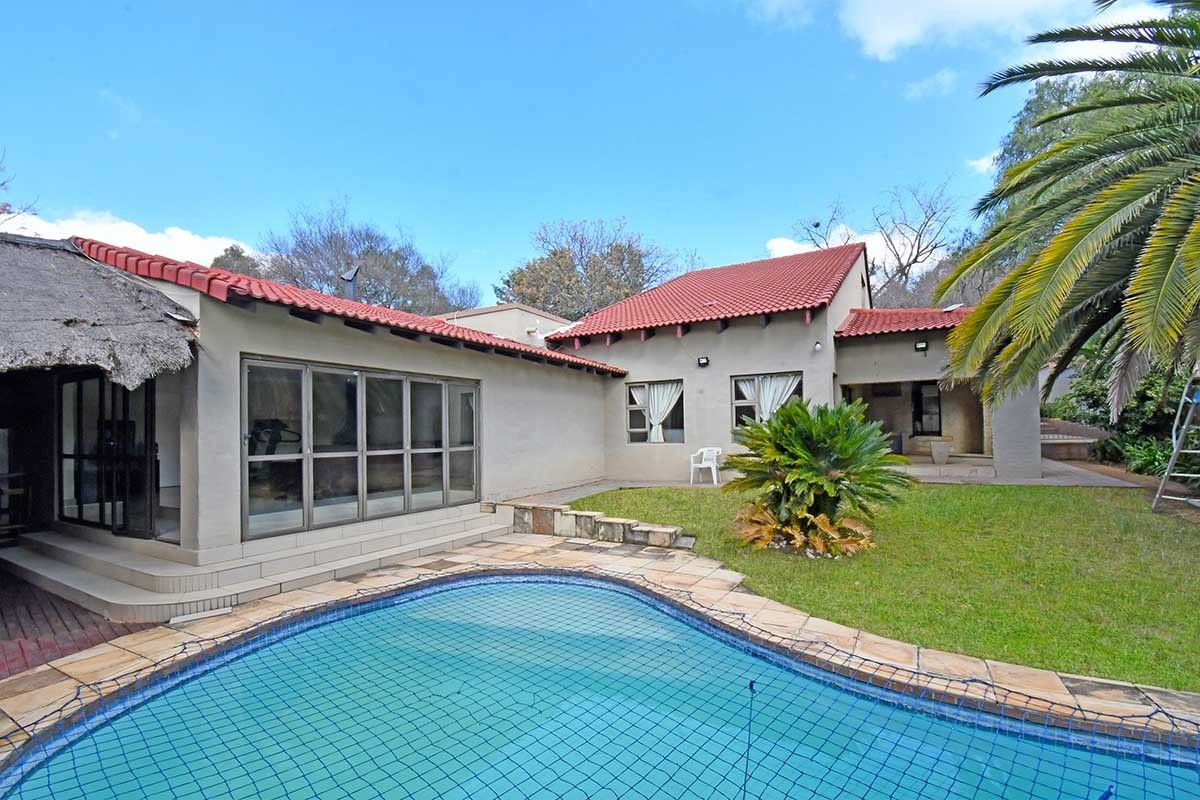 Rear view of the property featuring a swimming pool with safety net, landscaped garden, and a combination of tiled and thatched roof sections.