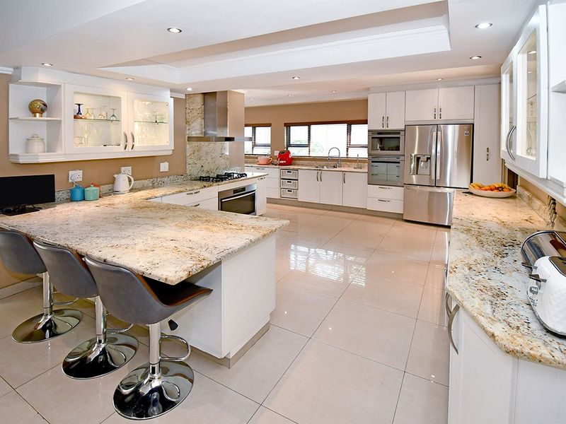 Spacious modern kitchen featuring granite countertops, high-end built-in appliances, ample cabinetry, and polished tiled flooring with recessed lighting.