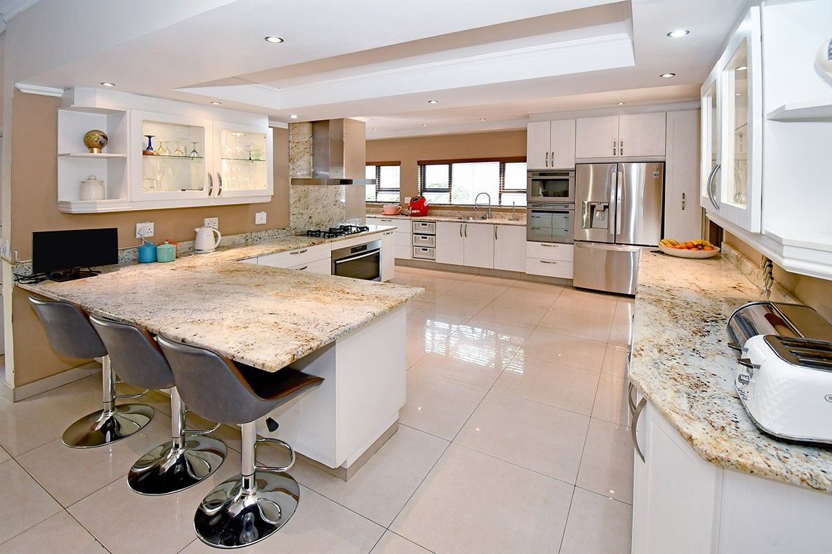 Spacious modern kitchen featuring granite countertops, high-end built-in appliances, ample cabinetry, and polished tiled flooring with recessed lighting.