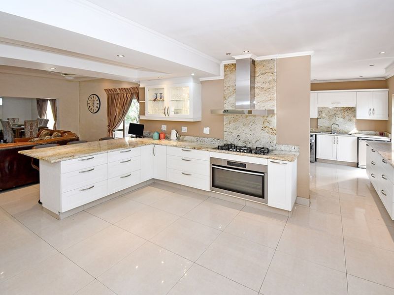 Spacious open-plan kitchen featuring granite countertops, built-in oven, gas hob, stainless steel extractor, and ample cabinetry, seamlessly flowing into the adjacent living area.