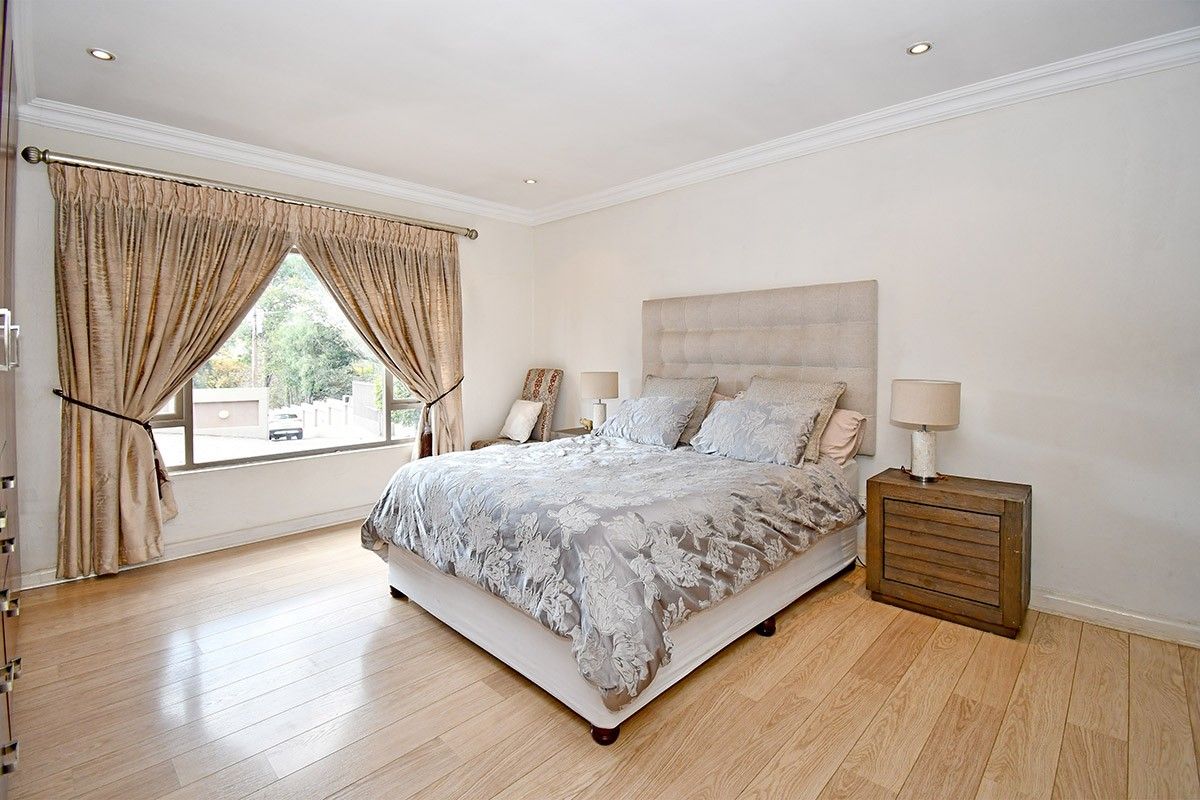 A well-maintained bedroom featuring light-toned laminate flooring, recessed downlighting, crown molding, and a built-in wardrobe.