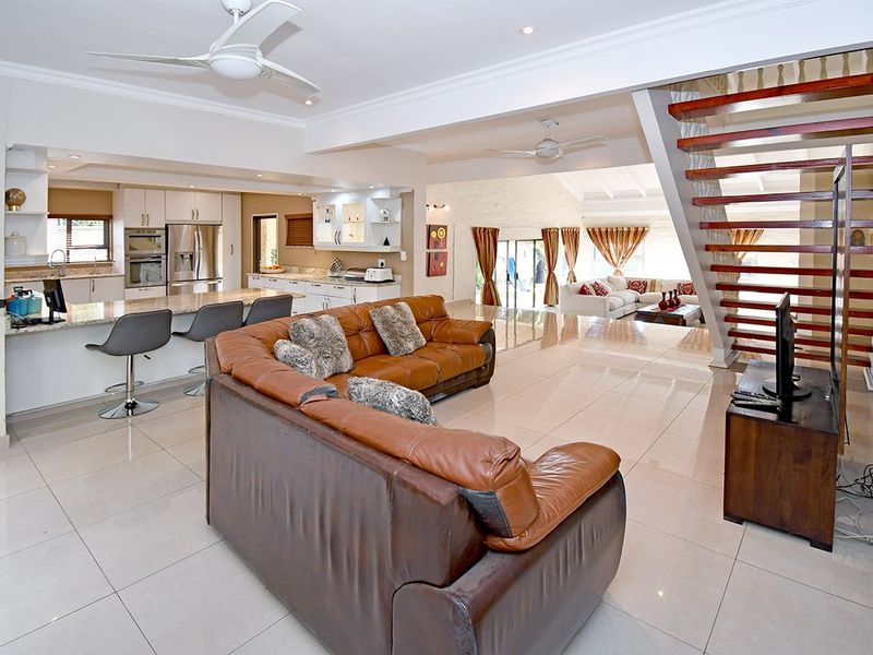 Spacious open-plan living area featuring a modern kitchen with granite countertops, tiled flooring, and an open staircase leading to the upper level.
