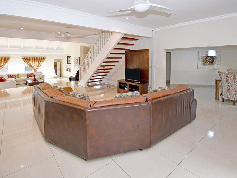 Spacious open-plan living area featuring large format floor tiles, a central staircase with wooden treads, and integrated ceiling fans.