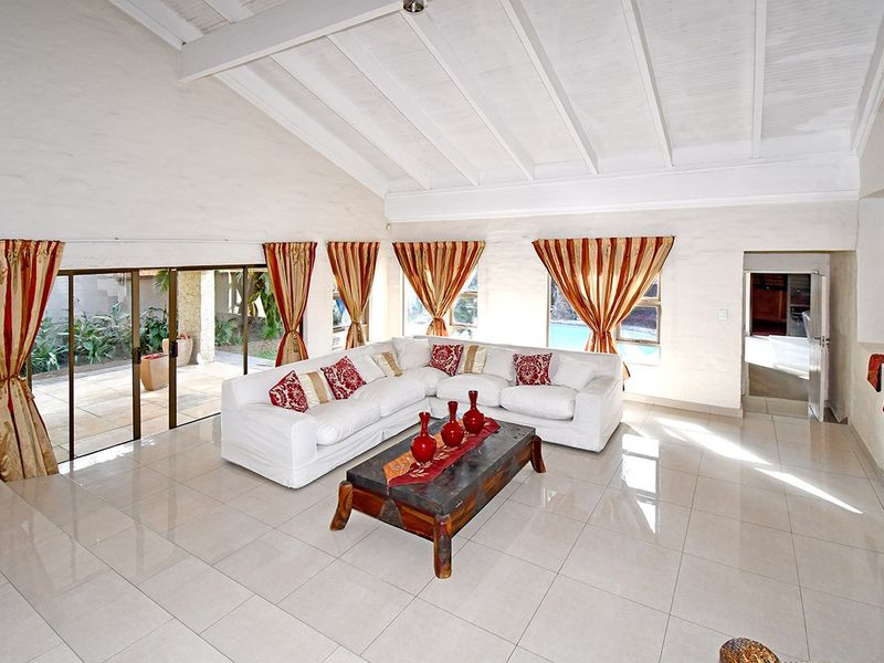 Spacious living room featuring a high vaulted ceiling with exposed beams, large windows, and tiled flooring, with direct access to the outdoor patio area.