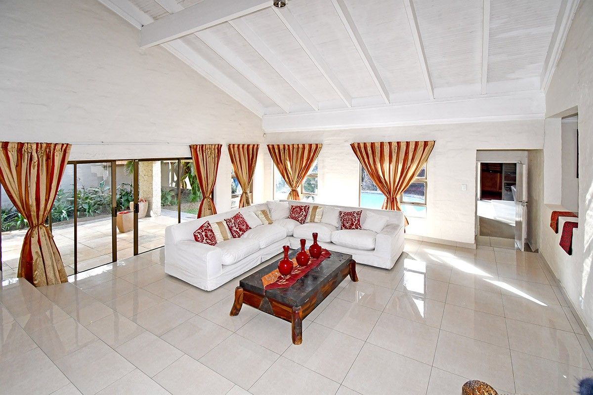Spacious living room featuring a high vaulted ceiling with exposed beams, large windows, and tiled flooring, with direct access to the outdoor patio area.
