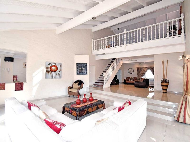 Spacious open-plan living area featuring a vaulted ceiling with exposed beams, a mezzanine level with a balustrade, and split-level tiled flooring.