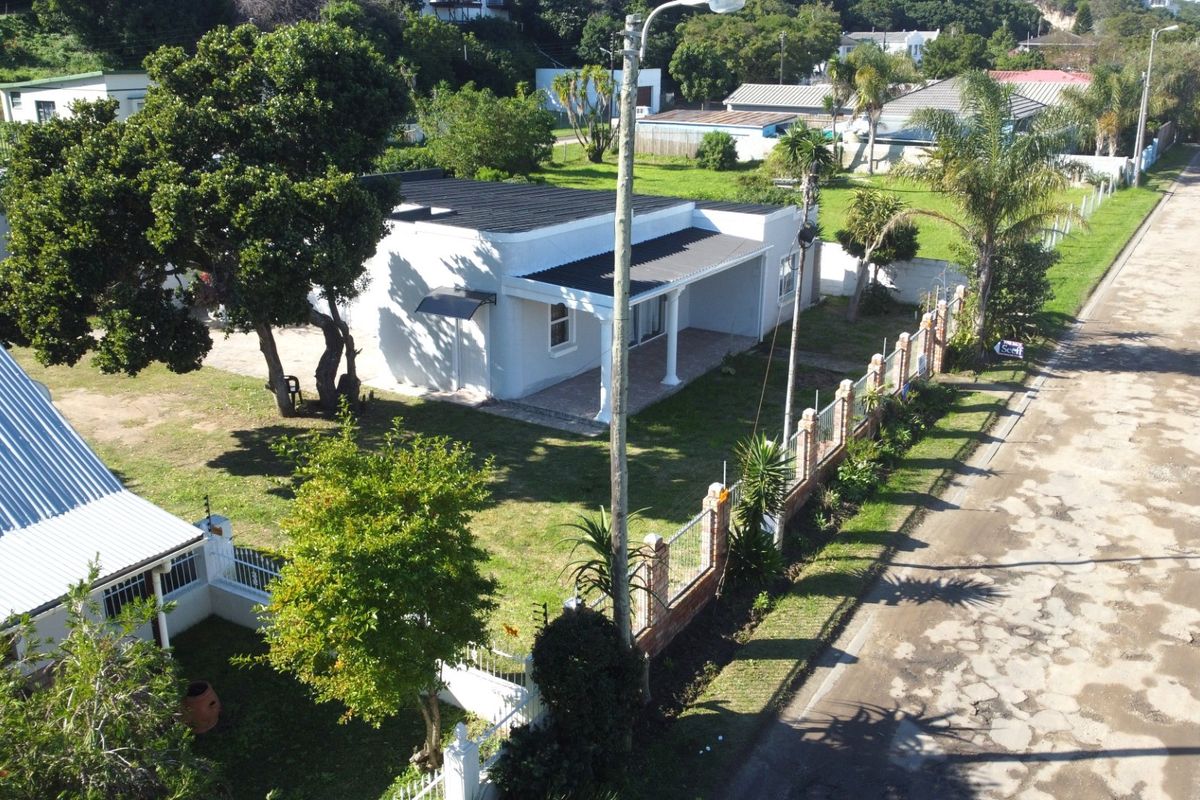 Aerial view of a residential property featuring a white house with a covered patio, large garden, and brick boundary wall along the street.
