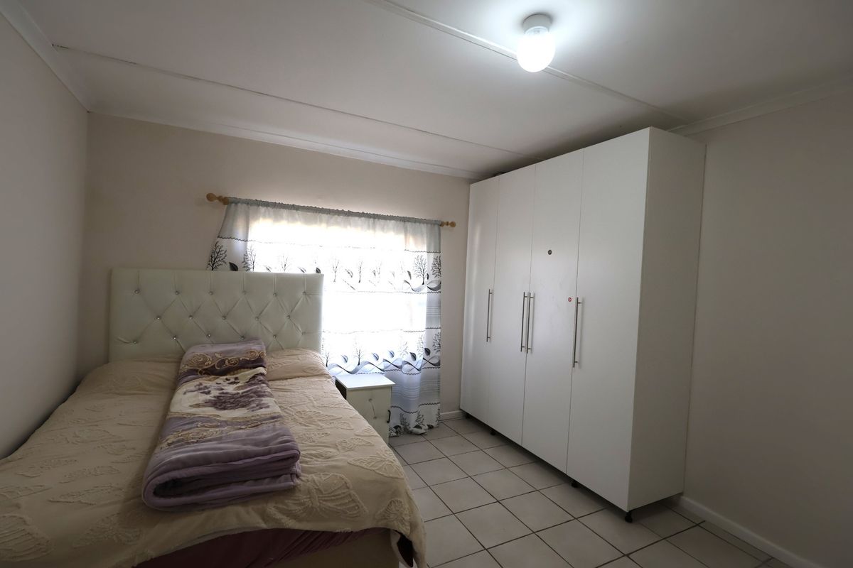 A functional bedroom featuring tiled flooring, a large white built-in wardrobe, and neutral wall finishes.