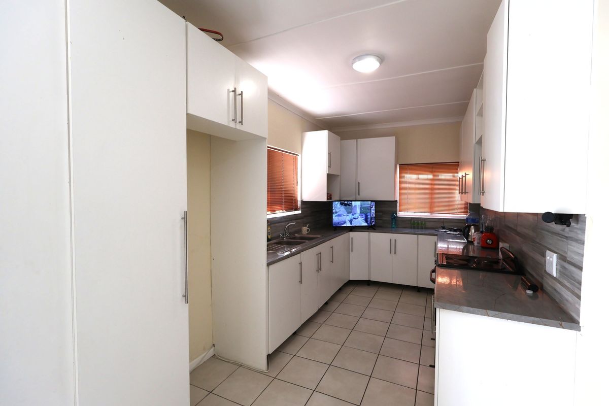 A functional kitchen featuring white cabinetry, laminate countertops, tiled flooring, and dual windows with venetian blinds.