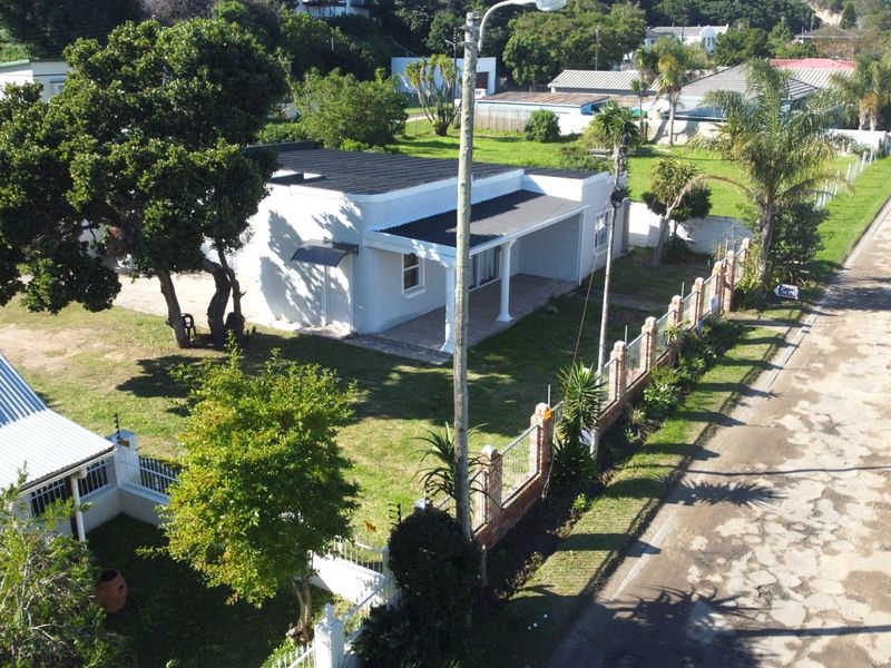 Aerial view of a residential property featuring a white house with a covered patio, large garden, and brick boundary wall along the street.