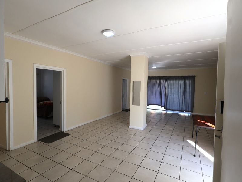 Spacious open-plan living area featuring neutral tiled flooring, a central structural column, and access to an outdoor space via sliding glass doors.