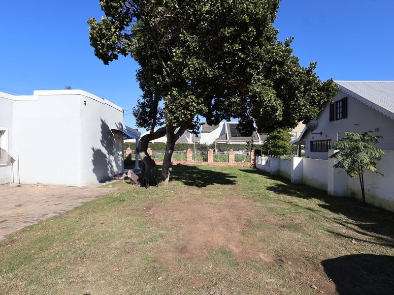 A spacious rear garden area featuring a paved section, a large mature tree, and perimeter boundary walls.