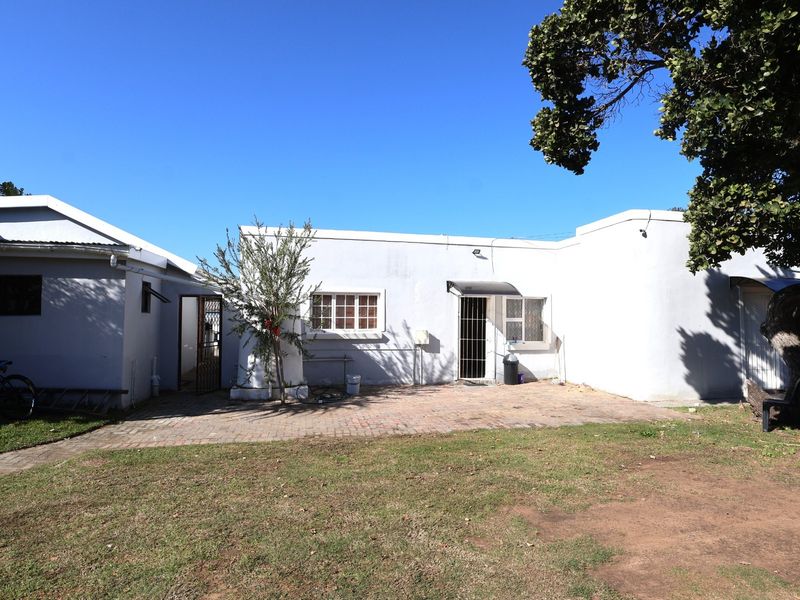 Rear view of the property featuring a paved patio area, lawn, and secure access points with security gates and bars.