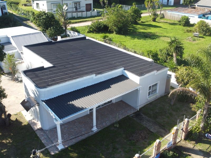 Aerial view of a residential property featuring a corrugated metal roof, a covered patio area, and a fenced garden.