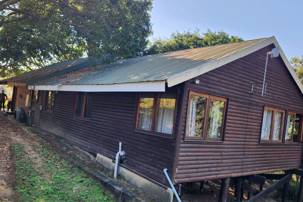 Side view of a timber log cabin structure featuring a corrugated metal roof, timber frame windows, and elevated stilt foundation.