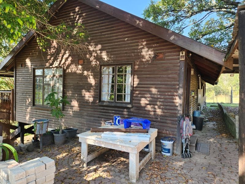 Rear view of a timber log cabin featuring a paved patio area and traditional wooden window frames.