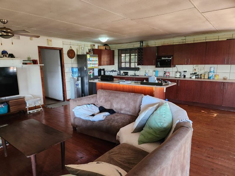 Open-plan living and kitchen area featuring wooden cabinetry, a central kitchen island, tiled backsplash, and wooden flooring throughout the space.