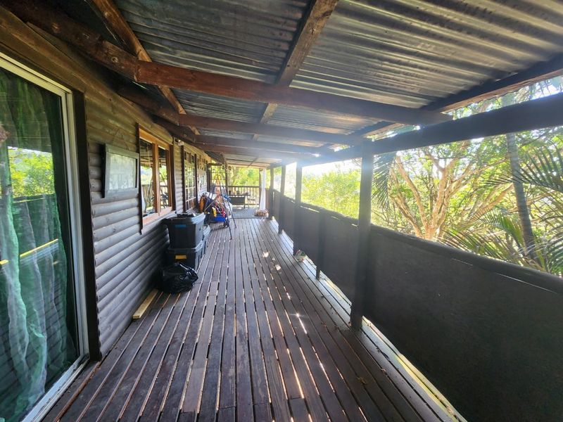 A covered timber balcony featuring a corrugated metal roof and wooden balustrade, offering an elevated outdoor space with natural surroundings.