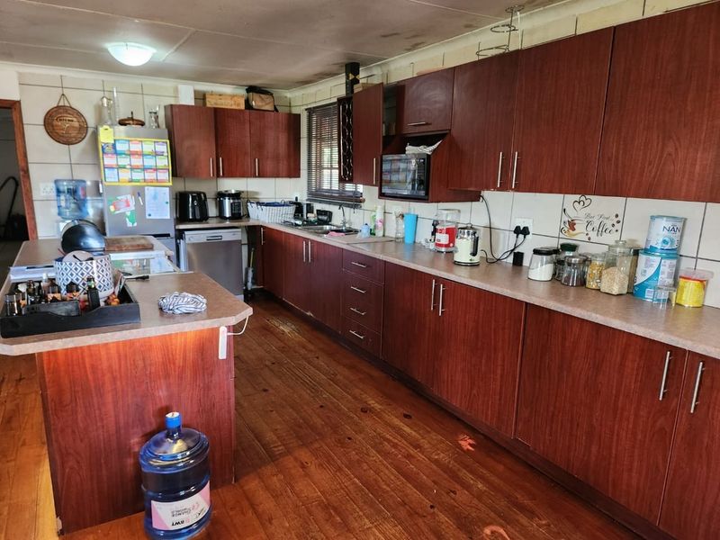 A functional kitchen featuring dark wood-look cabinetry, laminate countertops, a central island, and timber flooring, requiring some maintenance to the ceiling and floor finishes.