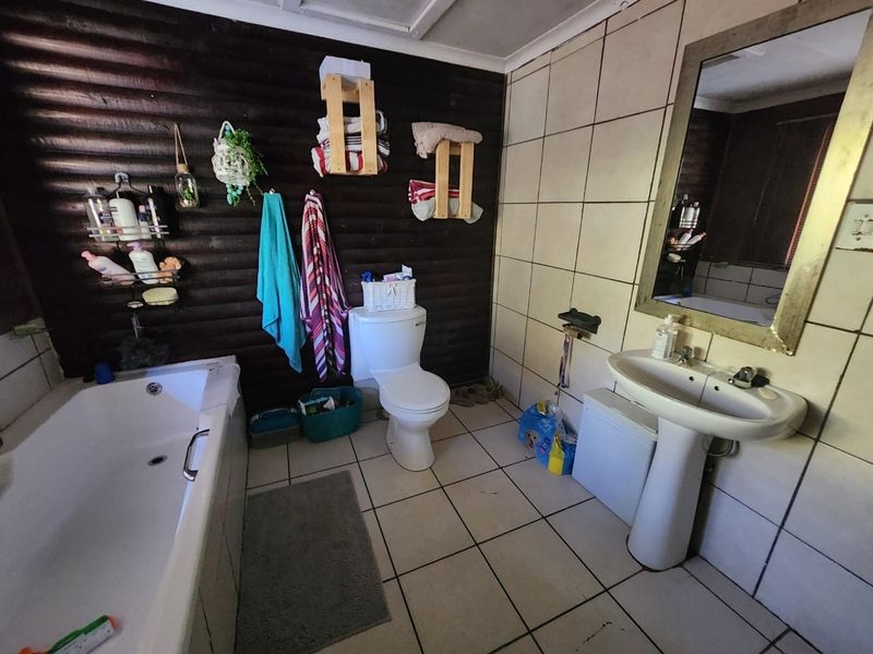 A functional bathroom featuring a bathtub, pedestal washbasin, and toilet, with tiled finishes and dark wood-paneled wall accents.