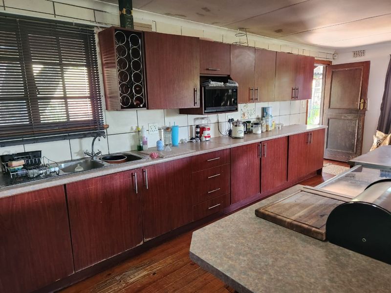 A functional kitchen featuring extensive timber cabinetry, laminate countertops, and a tiled backsplash, showing signs of wear and requiring cosmetic updates.
