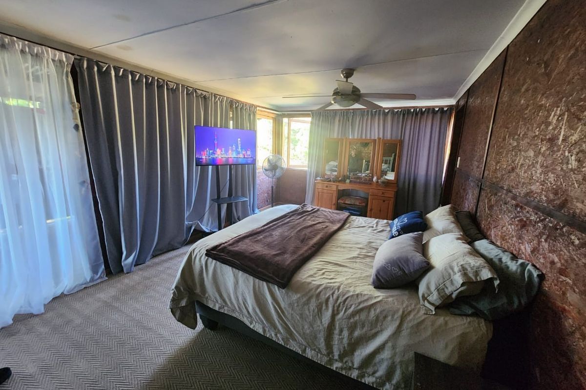 A bedroom featuring wood paneling, a ceiling fan, and large windows covered by curtains, offering a functional space with potential for cosmetic updates.