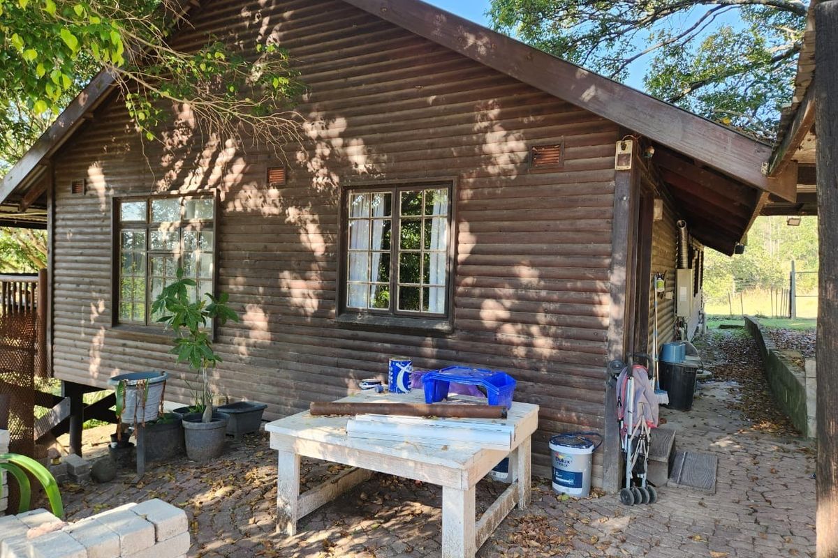 Rear view of a timber log cabin featuring a paved patio area and traditional wooden window frames.