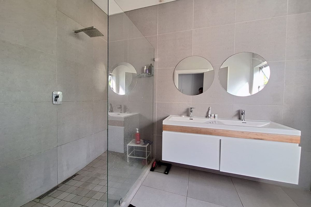 Modern bathroom featuring a spacious walk-in shower with glass screen, rain shower head, and a contemporary wall-mounted double vanity with integrated basins.