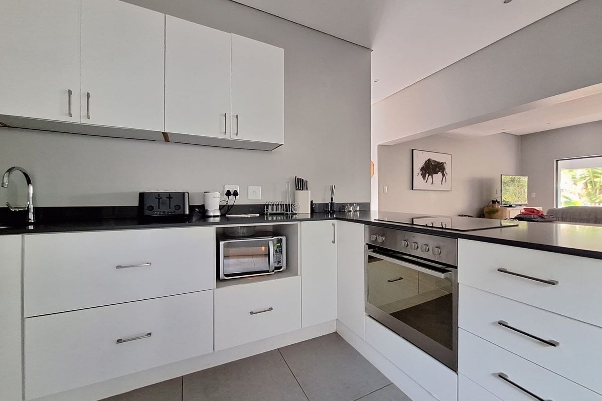 Modern kitchen featuring white cabinetry, dark stone countertops, integrated stainless steel oven, built-in microwave, and neutral floor tiles.