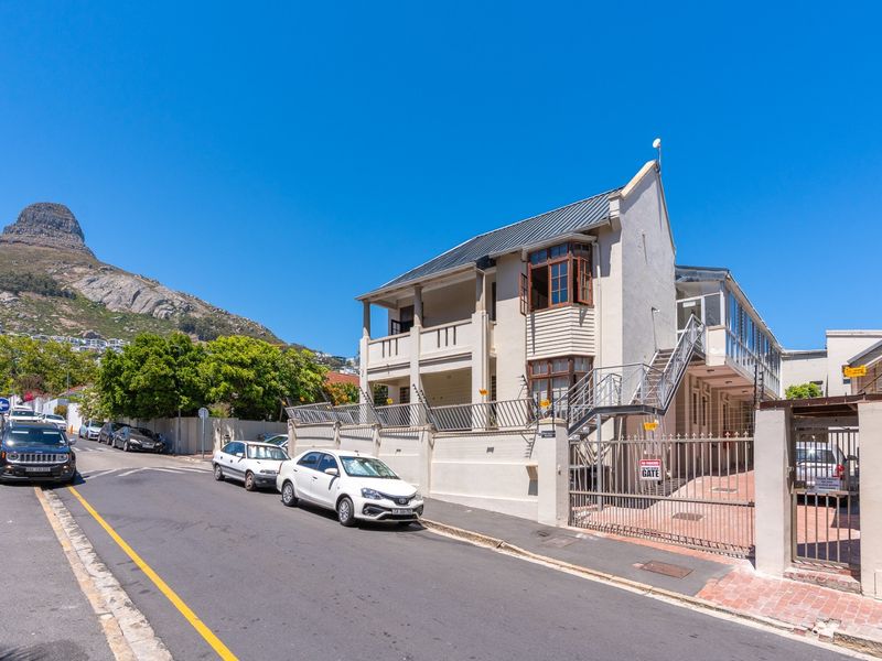 Exterior view of a multi-story apartment building featuring a metal security gate, external staircase, and balcony, situated on a street with mountain views.