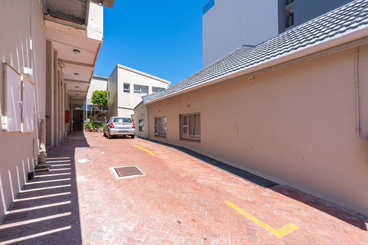A paved rear exterior area featuring a driveway, drainage infrastructure, and access to the building's side elevation.