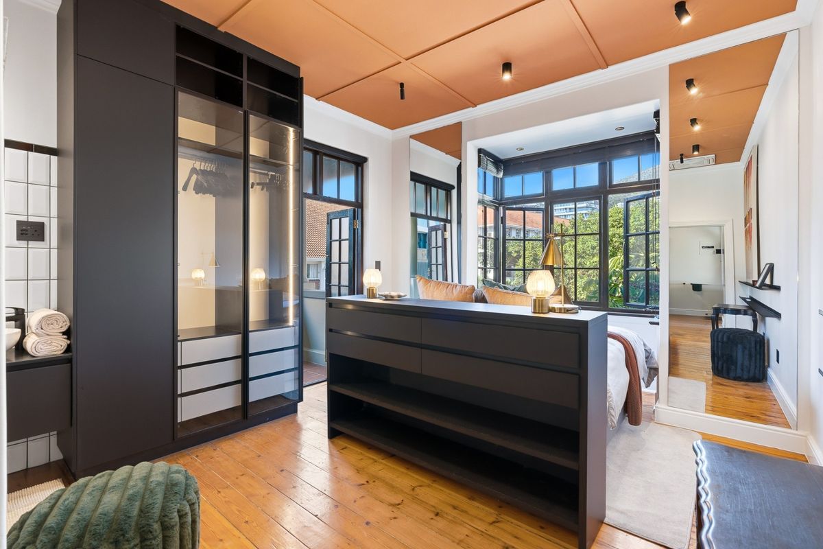 Modern bedroom featuring dark built-in cabinetry, hardwood flooring, and large casement windows with natural light, complemented by a unique painted ceiling.