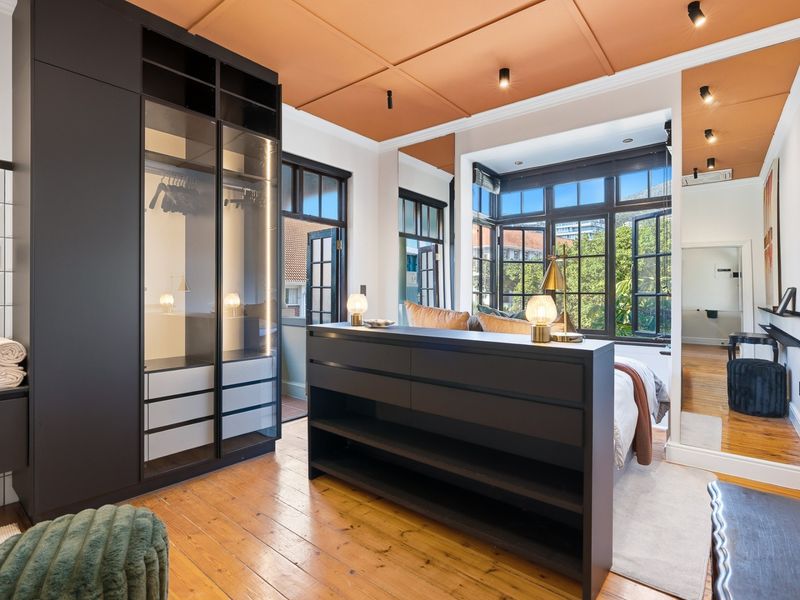 Modern bedroom featuring dark built-in cabinetry, hardwood flooring, and large casement windows with natural light, complemented by a unique painted ceiling.