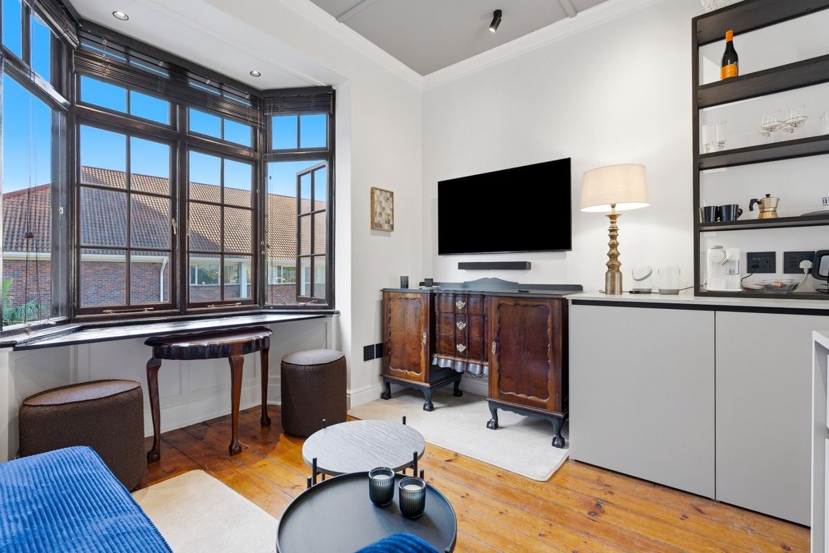 A well-maintained living room featuring polished timber flooring, a large bay window with dark frames, and built-in shelving units.